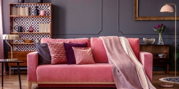 pink velvet sofa with dark painted walls and large gold bookcase