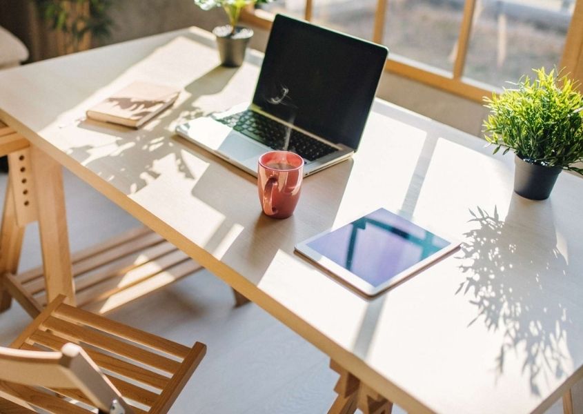 wooden desk with open laptop in front of large window