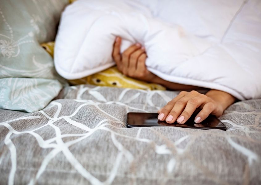 Woman under white duvet with her hand holding a mobile phone