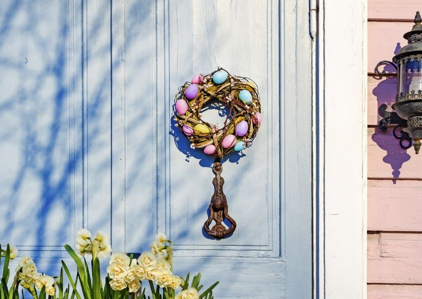 Blue wooden front door with Easter wreath featuring pink and blue painted eggs