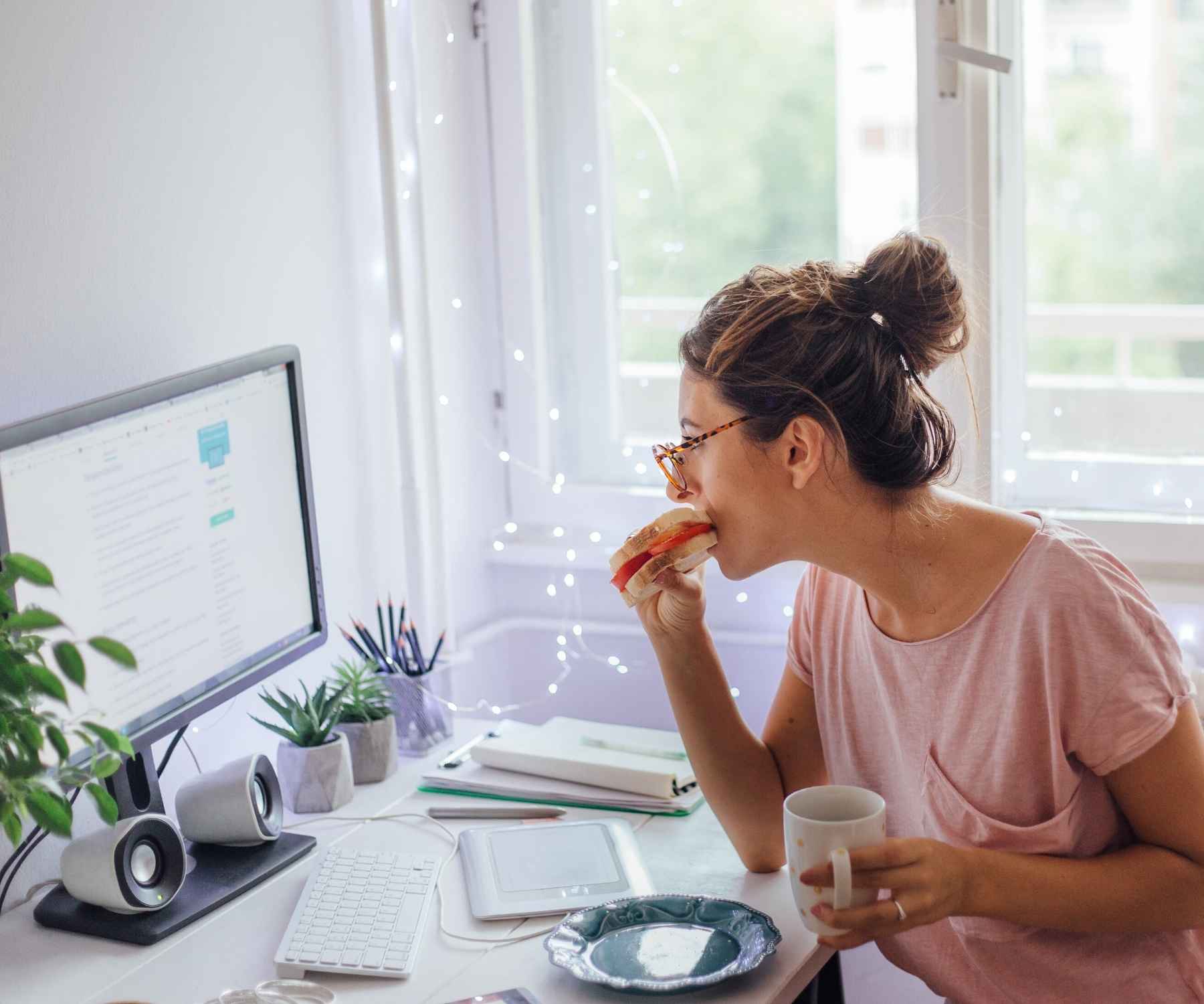 Woman eating toast at her desk in front of bright window