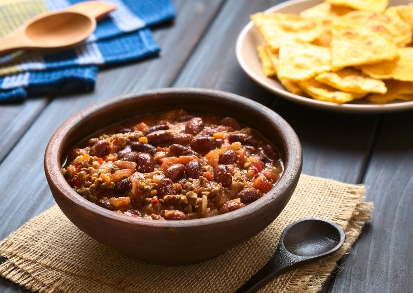 Bowl of chilli con carne on wooden table with tortilla chips