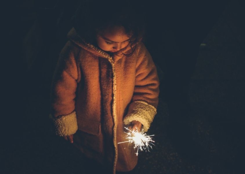 Young girl in thick coat holding sparkler in the dark