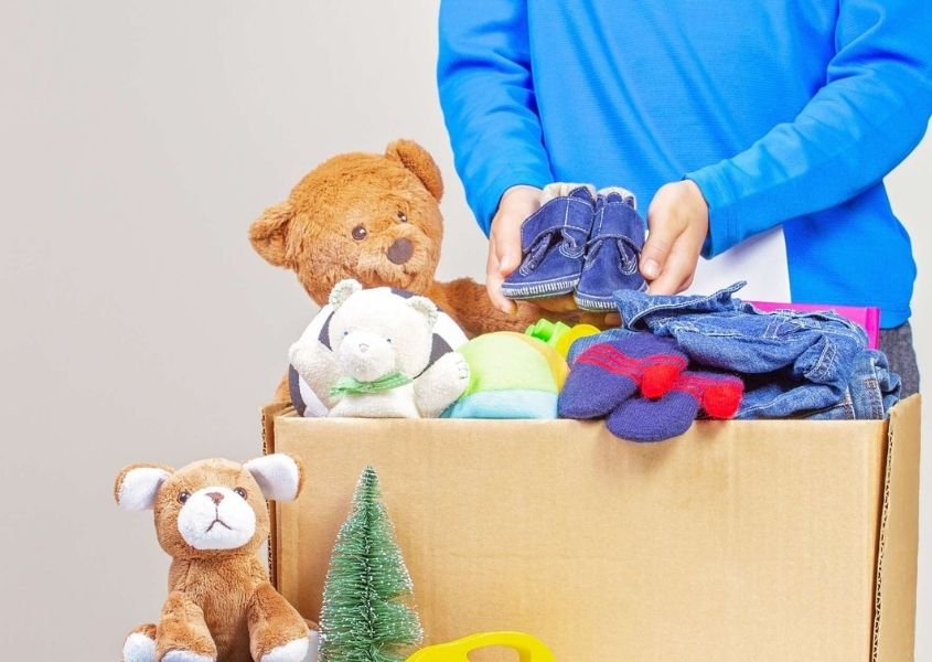Child in blue jumper holding cardboard box of toys