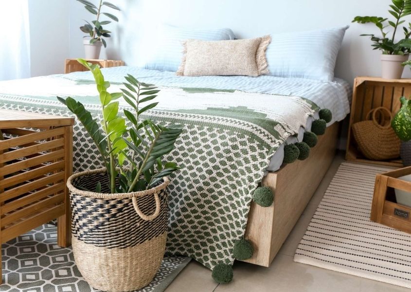 Plant in wicker basket at the foot of a wooden bed frame