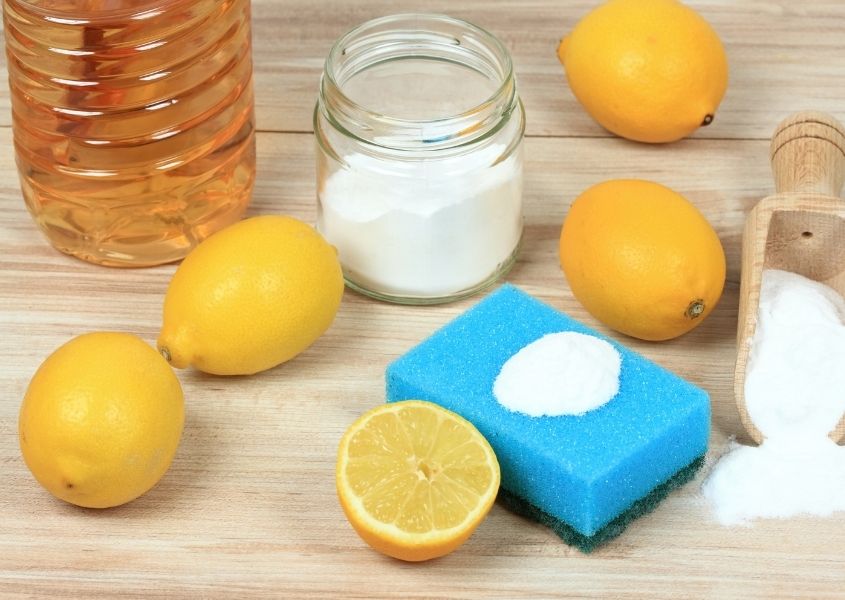 Whole and cut lemons with glass jar of white powder and plastic bottle of vinegar with a blue sponge
