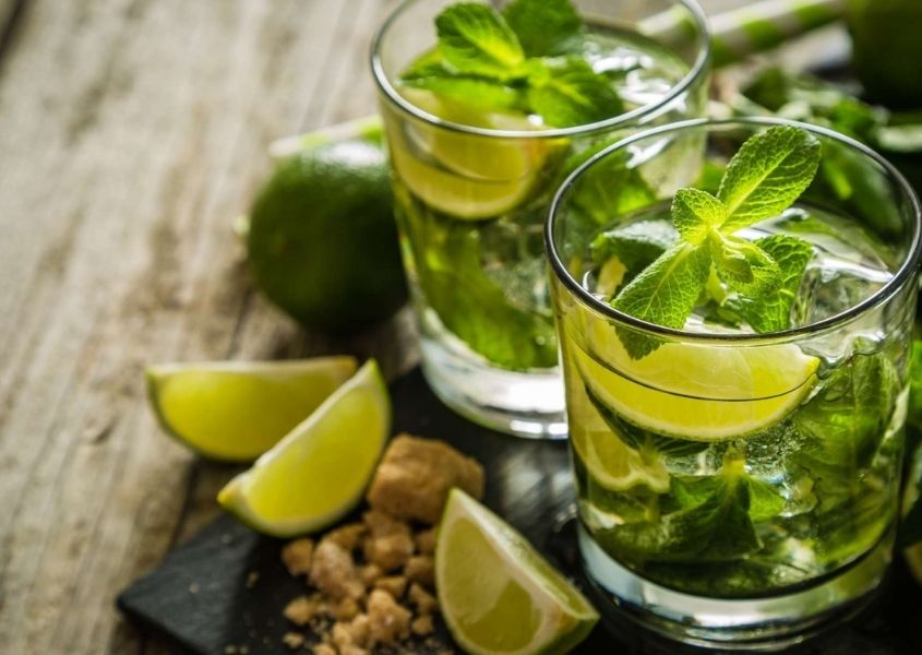 Two cocktails in tumblers with fresh mint and limes on wood background