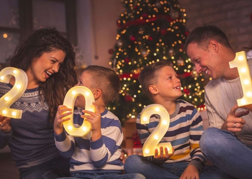Family of mum, dad and two children each holding a number spelling 2021 sitting on a sofa