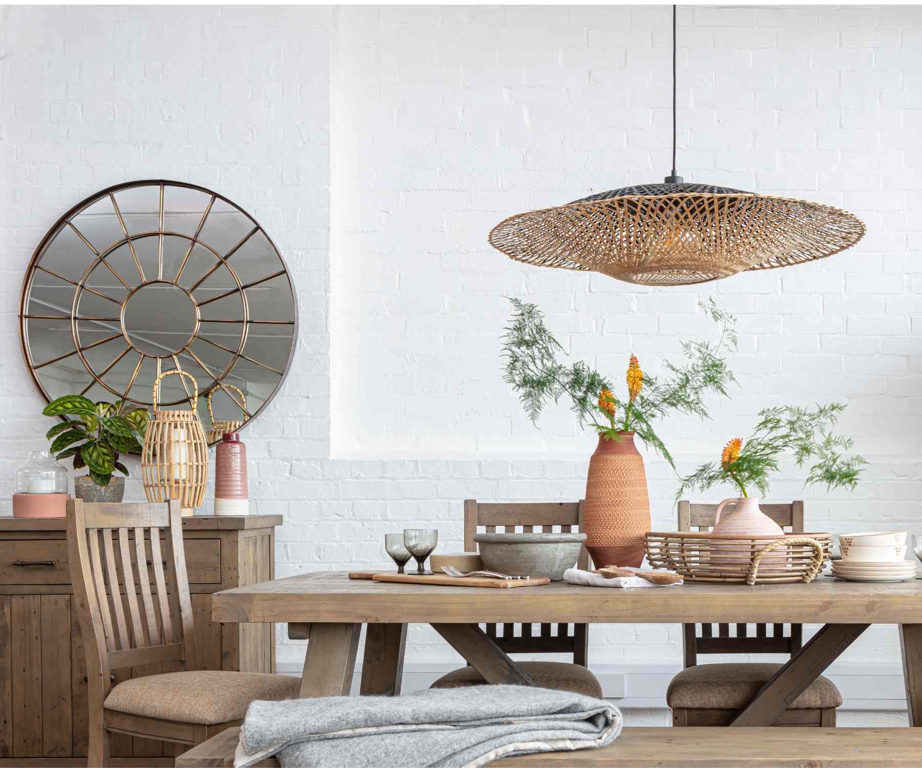 Round wall mirror next to reclaimed wood dining table with hanging pendant light