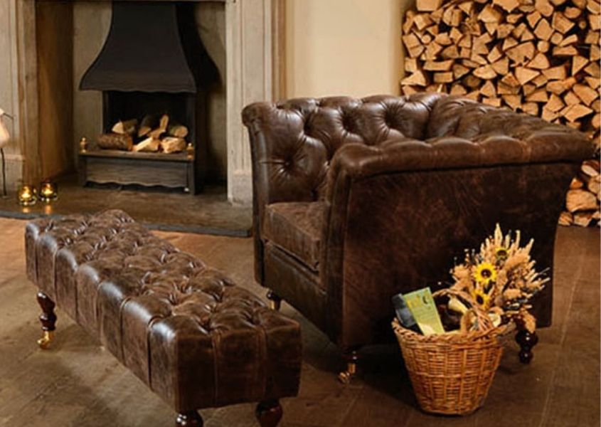 Brown leather chesterfield armchair and footstool in front of open fire