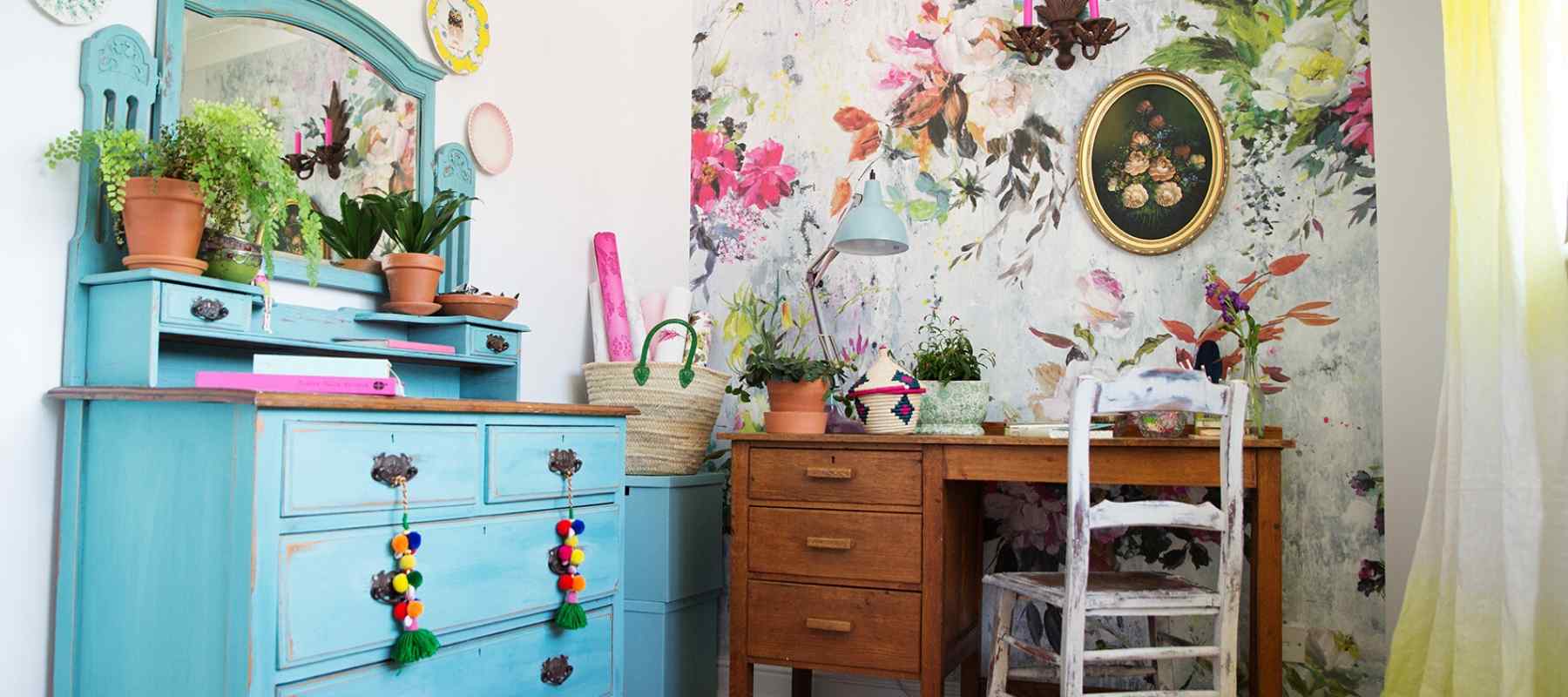 Blue painted chest of drawers with wooden desk and floral wallpaper