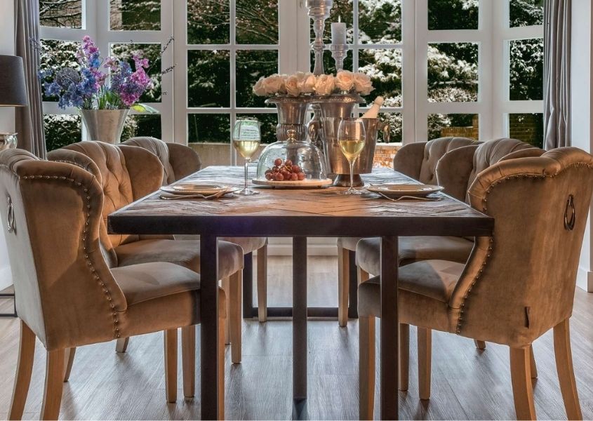Reclaimed wood dining table with velvet dining chairs and two glasses of white wine