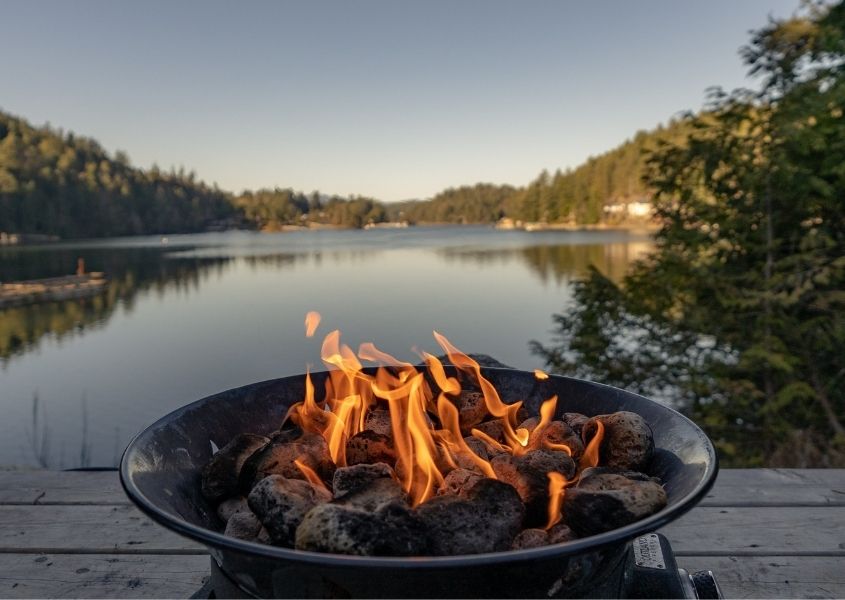 Round fire pit with flames next to a wide lake