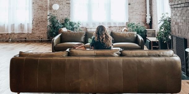 Girl sat on brown leather sofa facing a large warehouse window with exposed brick wall