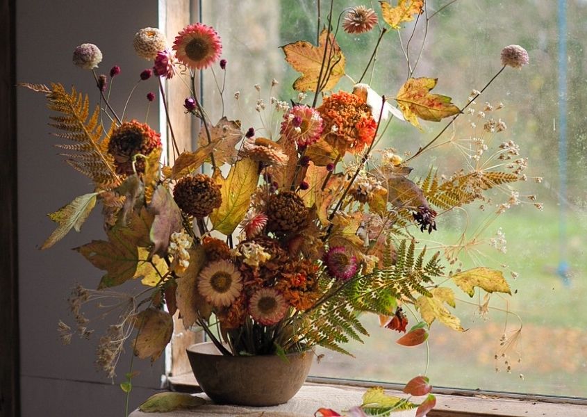 Brown vase with bouquet of dried flowers in front of window