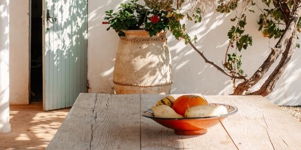 rustic dining table outdoors with orange bowl and large terracotta pot in the background