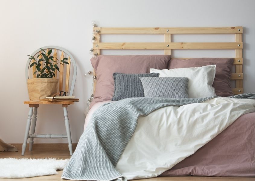 Wooden bed with palette headboard and painted wooden spindle chair with plant as bedsidetable