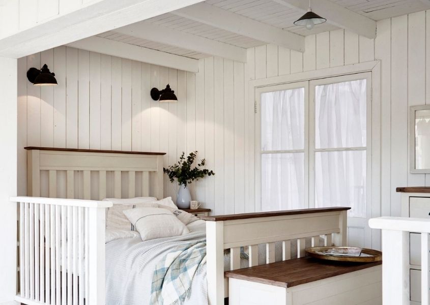 White bedroom with white panelled walls and wide wooden bed.