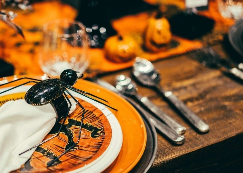 Halloween table decorations on wooden table with orange plates and large plastic spider 