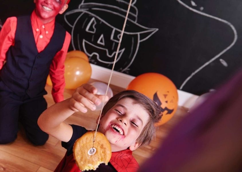 Two kids in Halloween costumes playing eat donut on string game