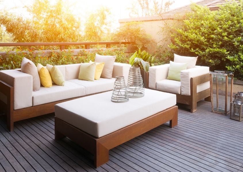 Outdoor sofa with white cushions and matching armchair and coffee table on wooden deck
