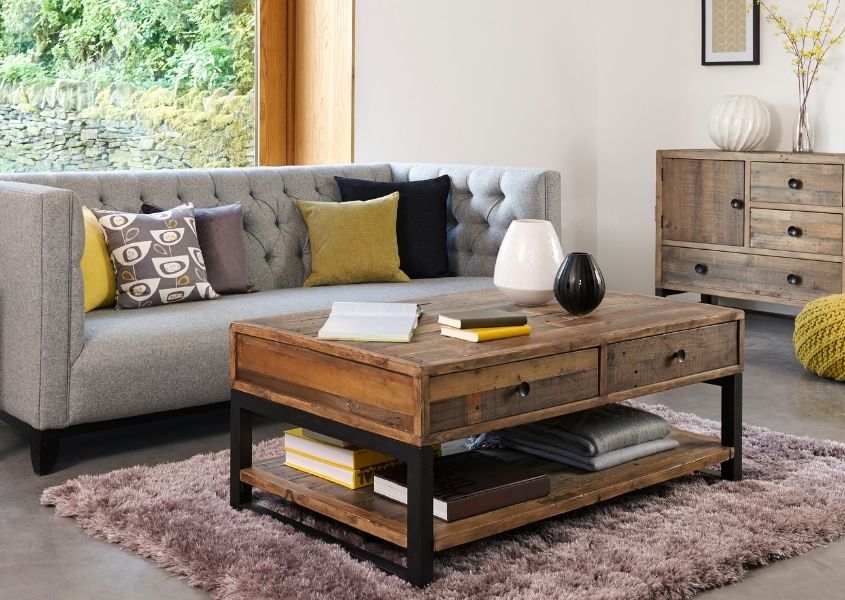 Reclaimed wood coffee table on grey rug with large grey sofa and yellow and grey cushions