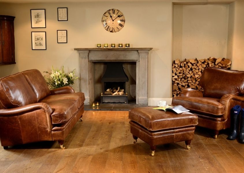 Rustic living room with large stone fireplace and brown leather sofa, brown leather armchair and matching leather footstool
