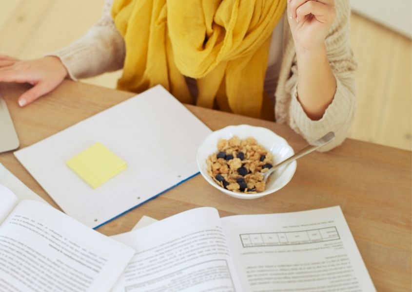 woman at wooden desk with books and bowl of cereal