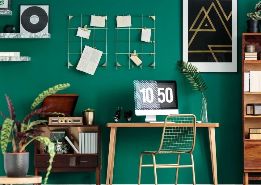 Wooden home office desk against an aqua green wall with gold metal pin board on the wall
