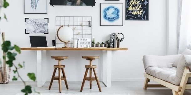 Home office desk with two wooden stools and gallery of prints on the wall