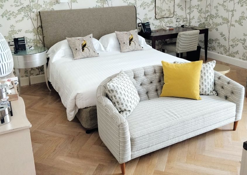 Small grey sofa at foot of a double bed with white covers