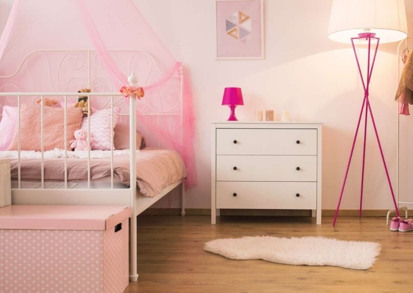 Pink children's bedroom with white metal bed, white chest of drawers and sheepskin rug on wooden floor