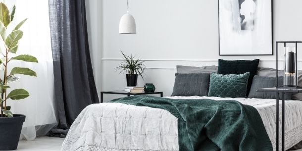 Modern bedroom with large bed with white and dark green covers and cushion. Room also features tall houseplant