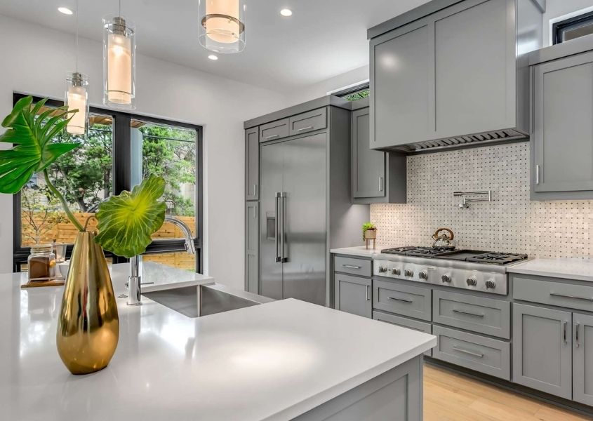 Grey modern kitchen with white stone worktops and gold vase with large green tropical leaf on top