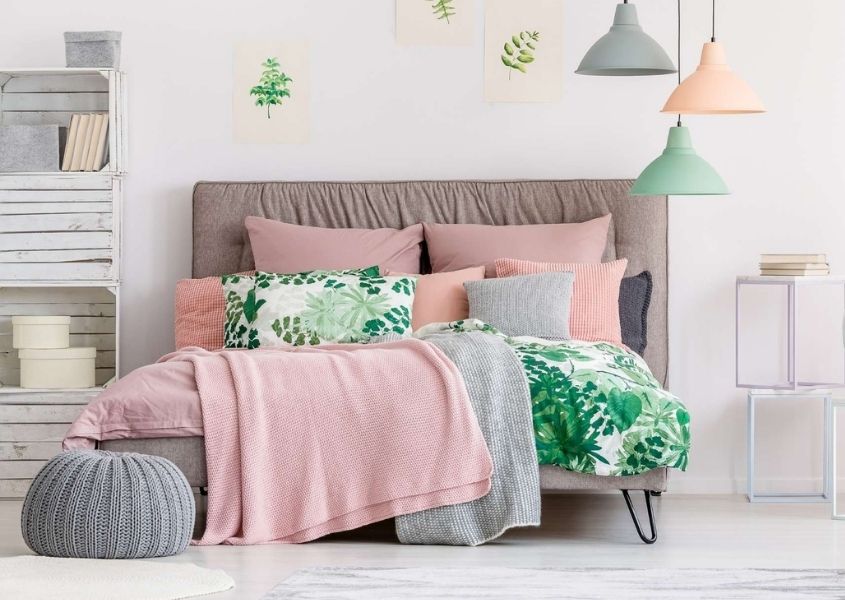 Pastel coloured bedroom with pale pink upholstered bed, pink covers and grey, pink and green hanging ceiling lights