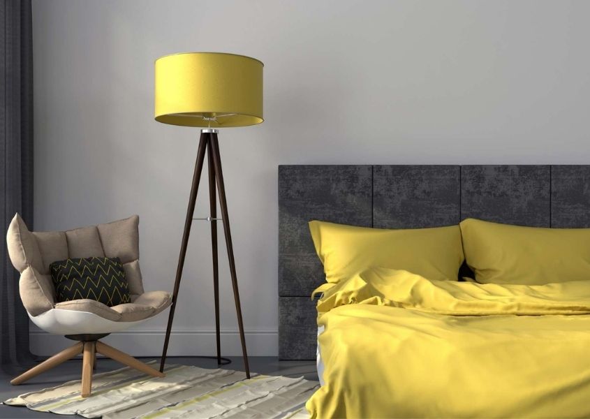 Bedroom with grey upholstered bed and bright yellow covers and yellow floor lamp