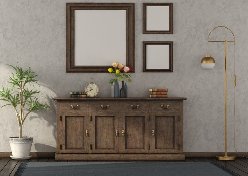 Wooden sideboard with trio of mirrors on wall above and a gold floor lamp and plant in room