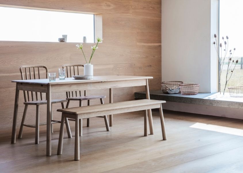 Pale wooden dining table with wooden bench in room with wood wall and floor